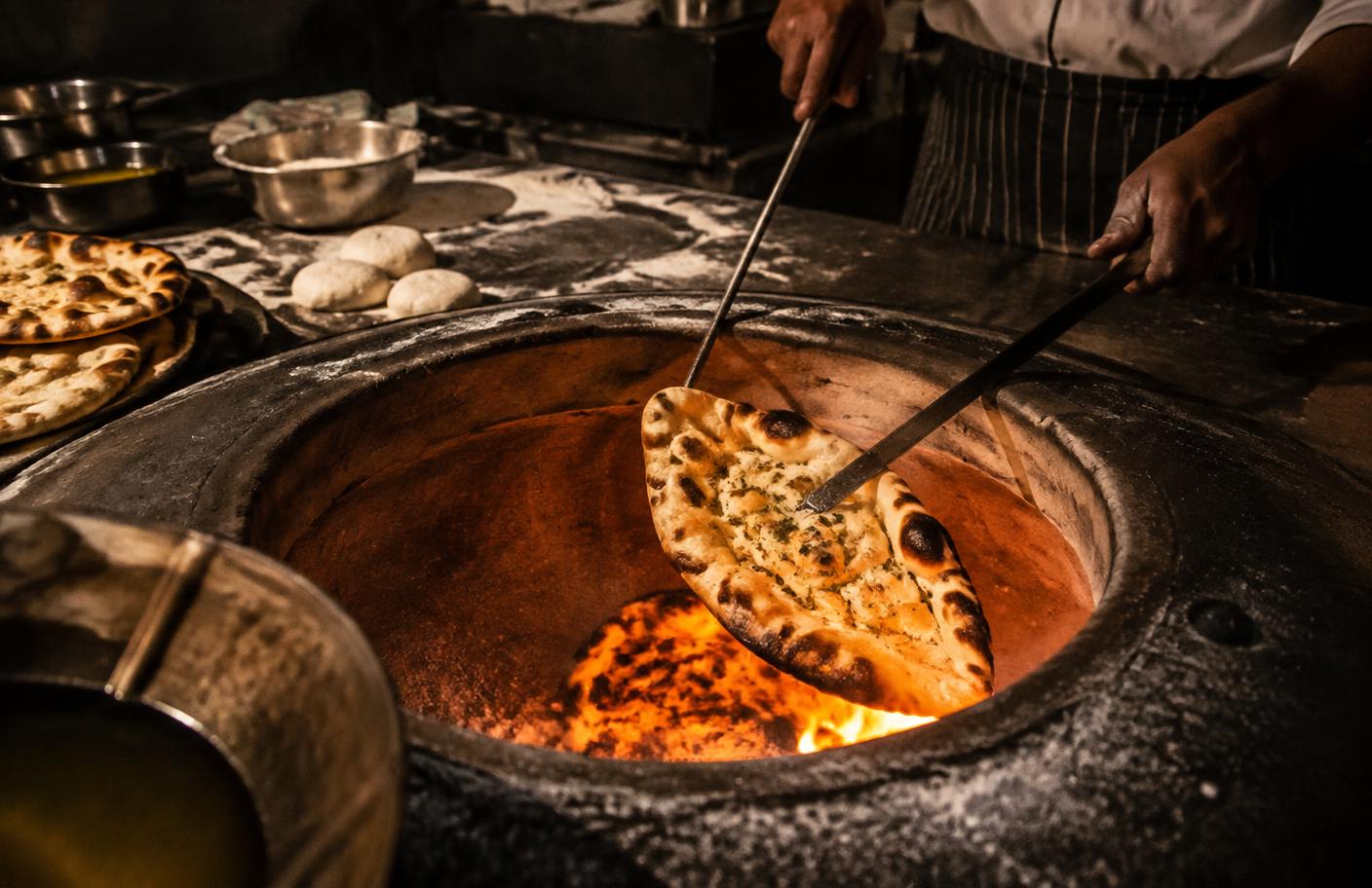 Chef baking naan in a clay tandoor